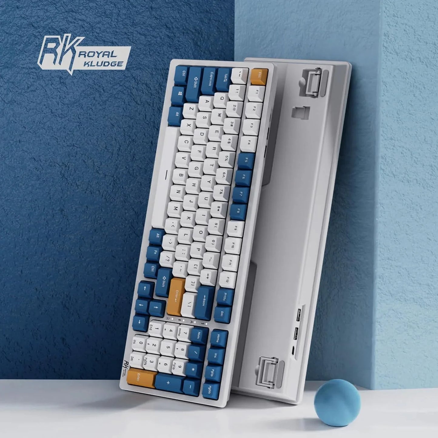 Royal Kludge mechanical keyboard with white, blue, and orange keycaps against blue textured walls and a light blue ball