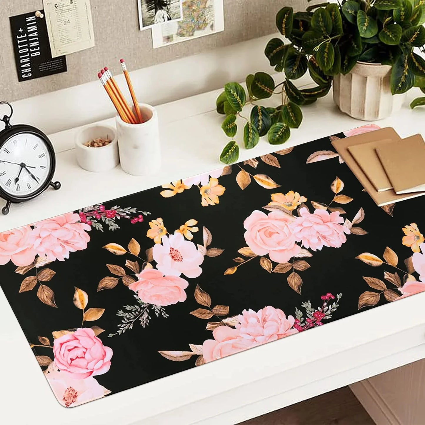 Floral desk mat with pink and peach flowers on black background, decorated workspace with pencils, clock, plant