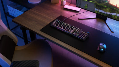 RGB gaming keyboard and mouse on a desk with ergonomic chair, large monitor, modern setup