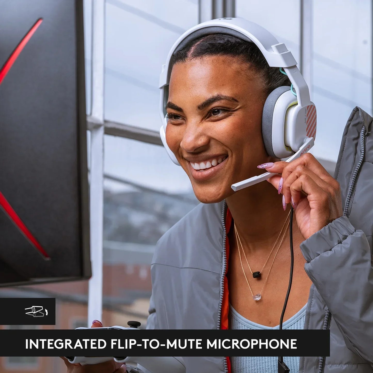 Smiling woman wearing white gaming headset with flip-to-mute microphone, holding controller setup by window