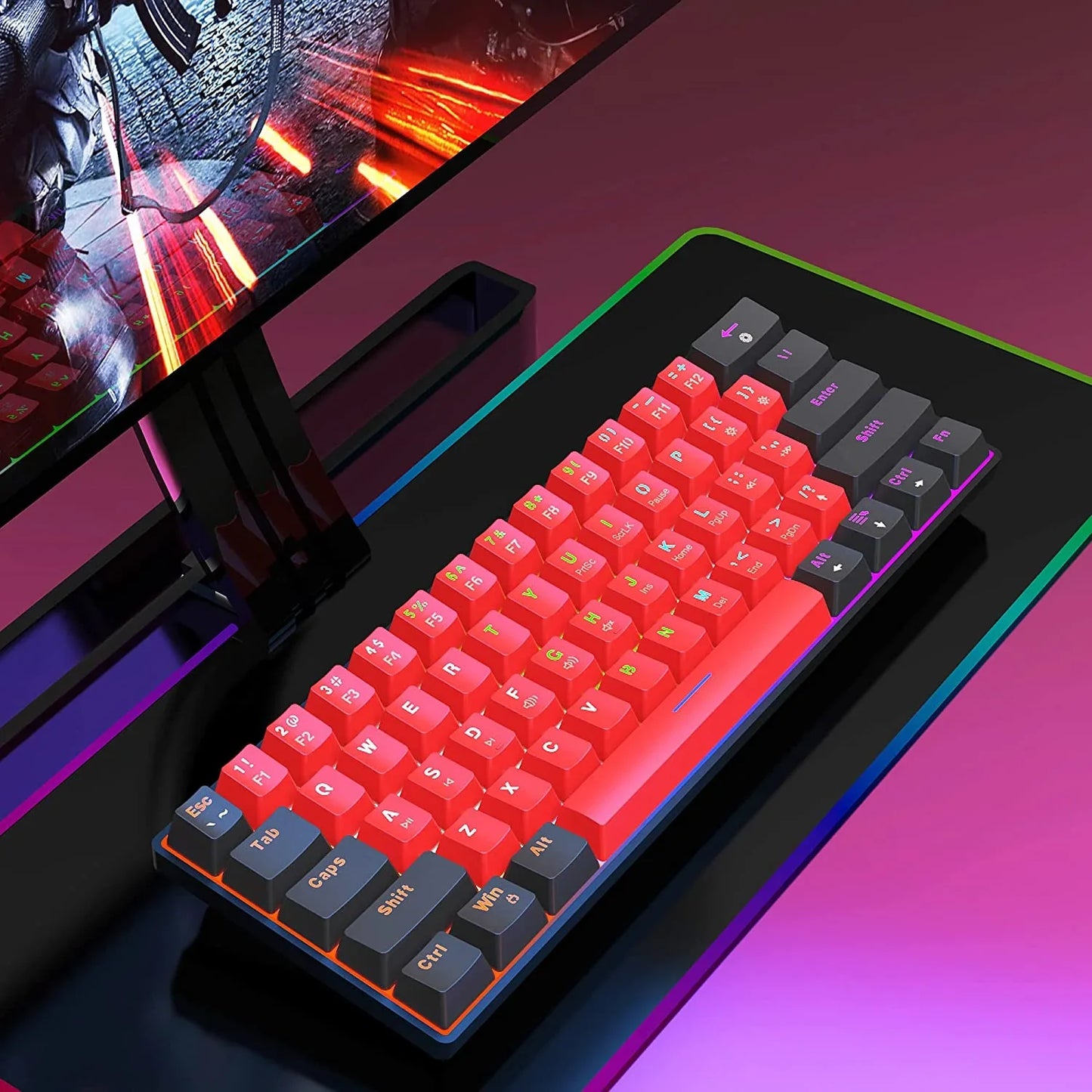Compact mechanical gaming keyboard with vibrant red and gray keycaps, RGB lighting on black desk next to a gaming monitor