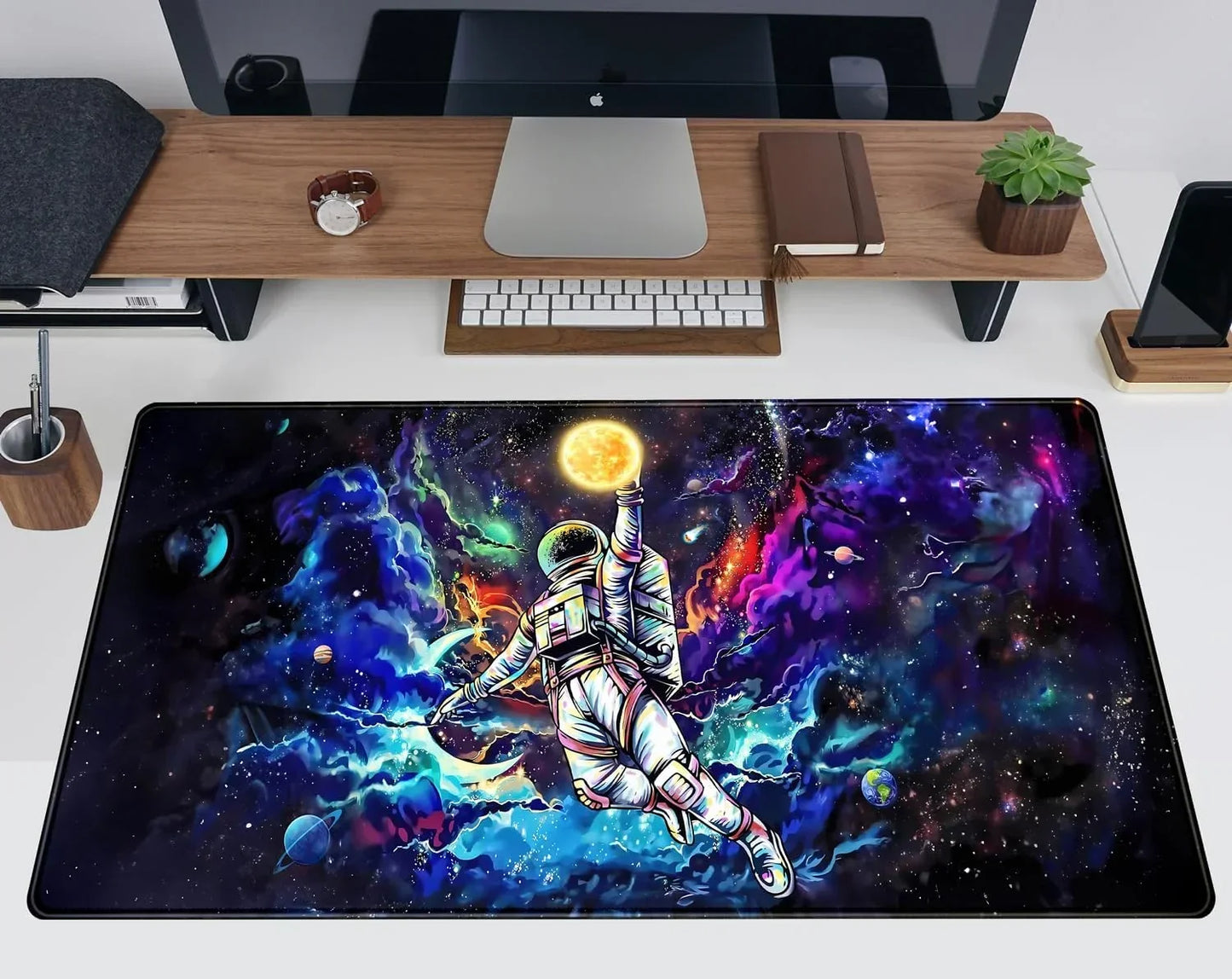 Desk setup with a colorful space-themed gaming mouse pad featuring an astronaut reaching for a glowing sun among planets