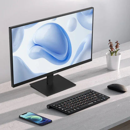 Modern desktop setup with widescreen monitor, wireless keyboard, mouse, smartphone, and small potted plant