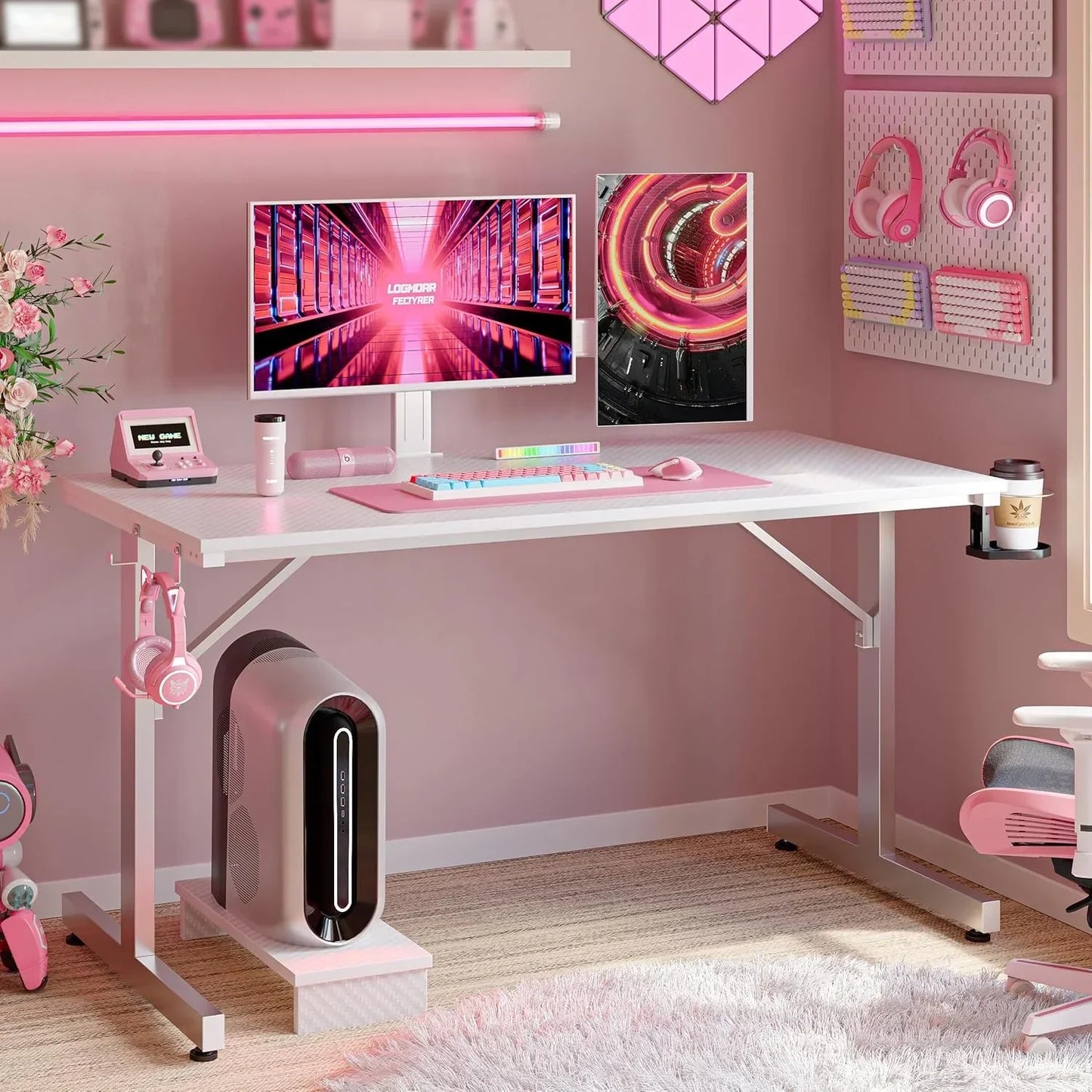 Pink-themed gaming desk setup with dual monitors, pink keyboard, headphones, and PC tower under white desk