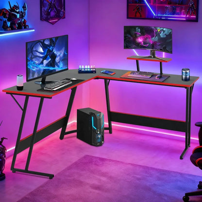 Modern L-shaped black and red gaming desk setup with dual monitors, RGB lighting, desktop PC, gaming keyboard, mouse, and gaming accessories