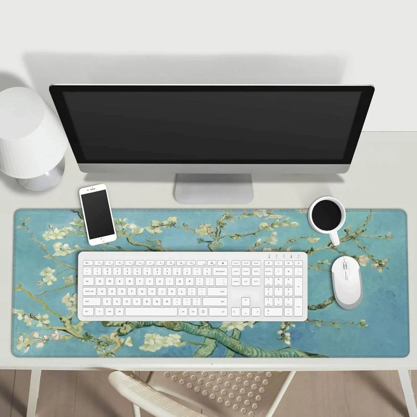 Minimalist workspace with desktop monitor, white keyboard and mouse on blue botanical desk mat, smartphone and coffee cup