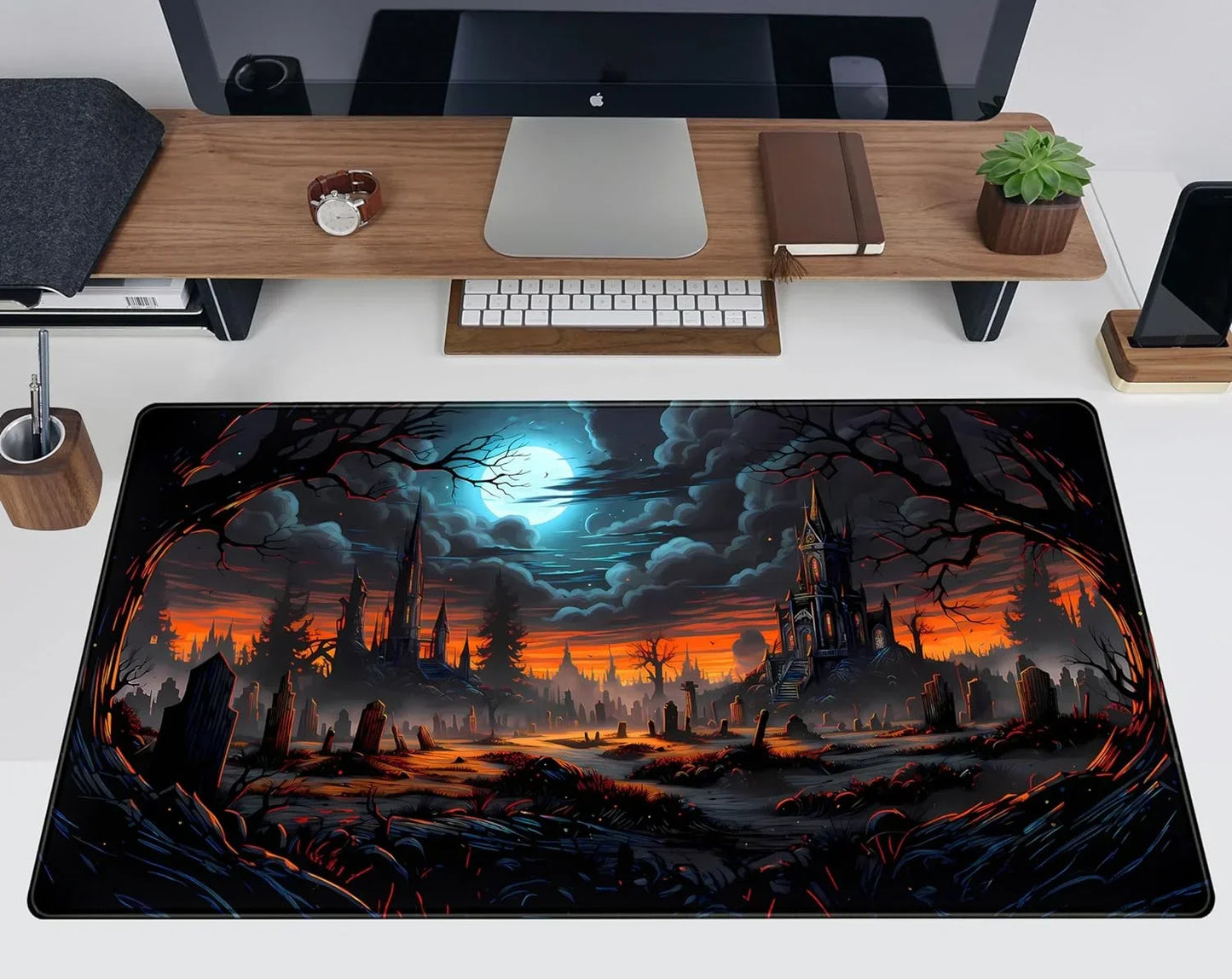 Gaming desk setup with spooky moonlit cemetery and gothic castle mousepad, sleek computer and wooden desk accessories