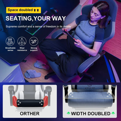 Woman sitting cross-legged on a gray ergonomic gaming chair in a colorful room with keyboard and mouse on desk