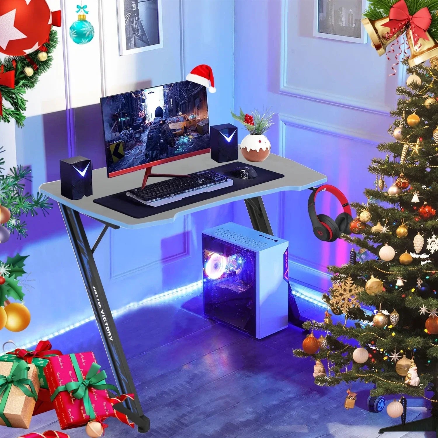 Modern gaming desk setup with curved monitor, PC tower with RGB lighting, speakers, keyboard, mouse, and Christmas decor