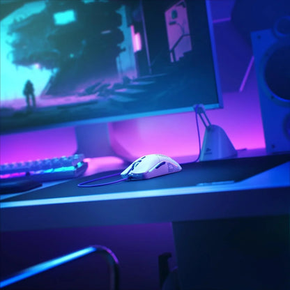 White wired gaming mouse on black mousepad in a blue and purple lit gaming setup with monitor and keyboard