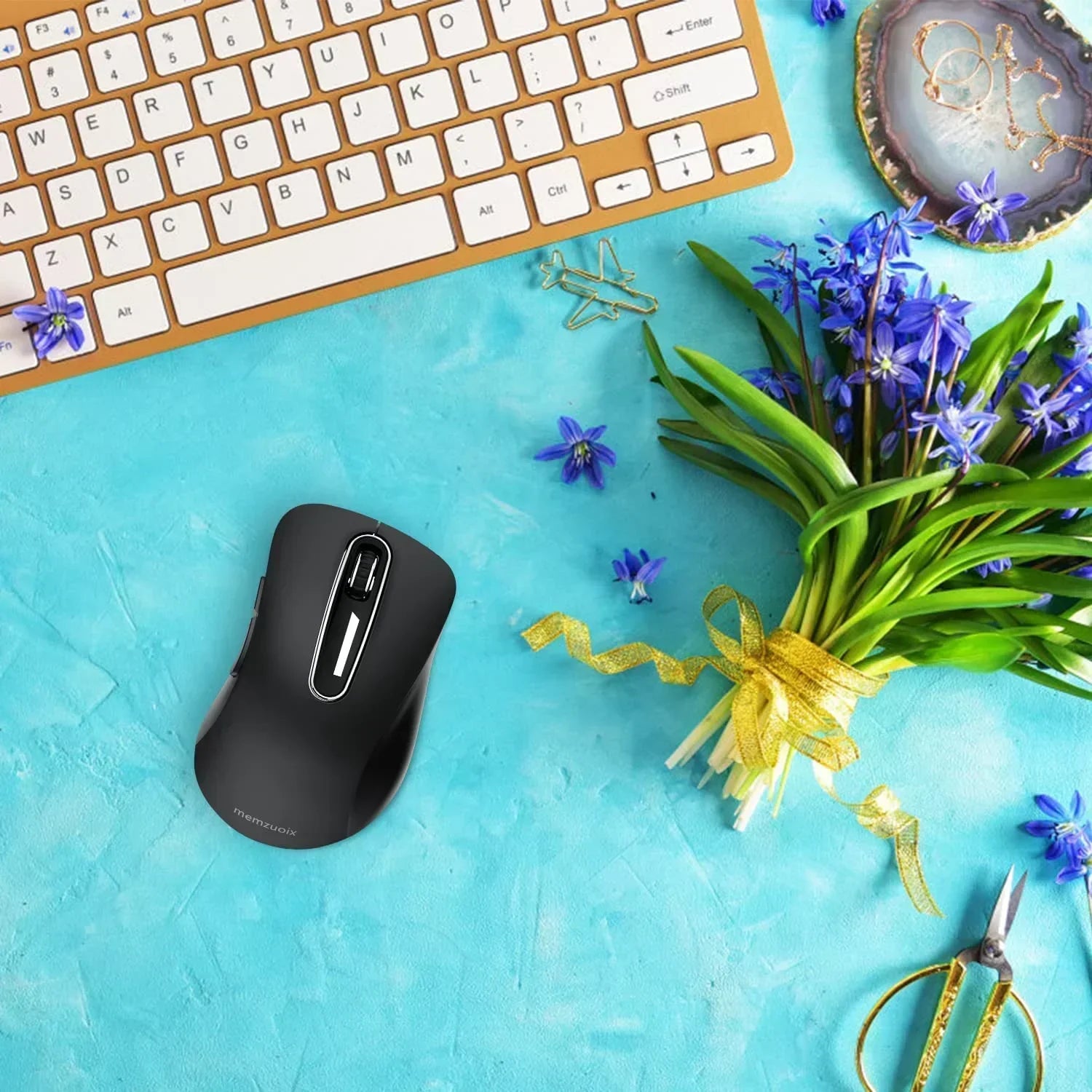 Wireless ergonomic gaming mouse on a blue desk with keyboard, flowers, and accessories