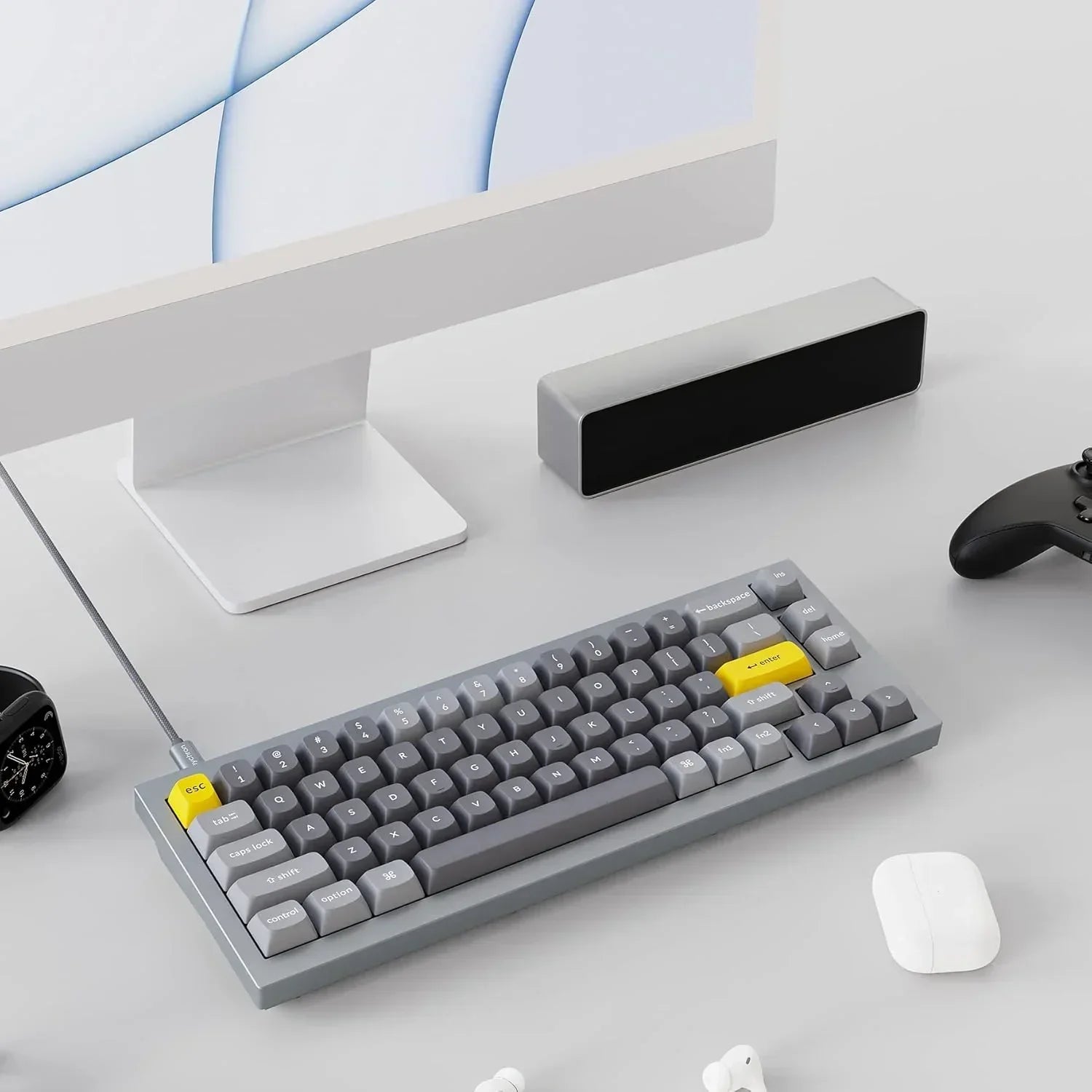 Modern gaming setup with gray mechanical keyboard, yellow keycaps, monitor, controller, and desk accessories