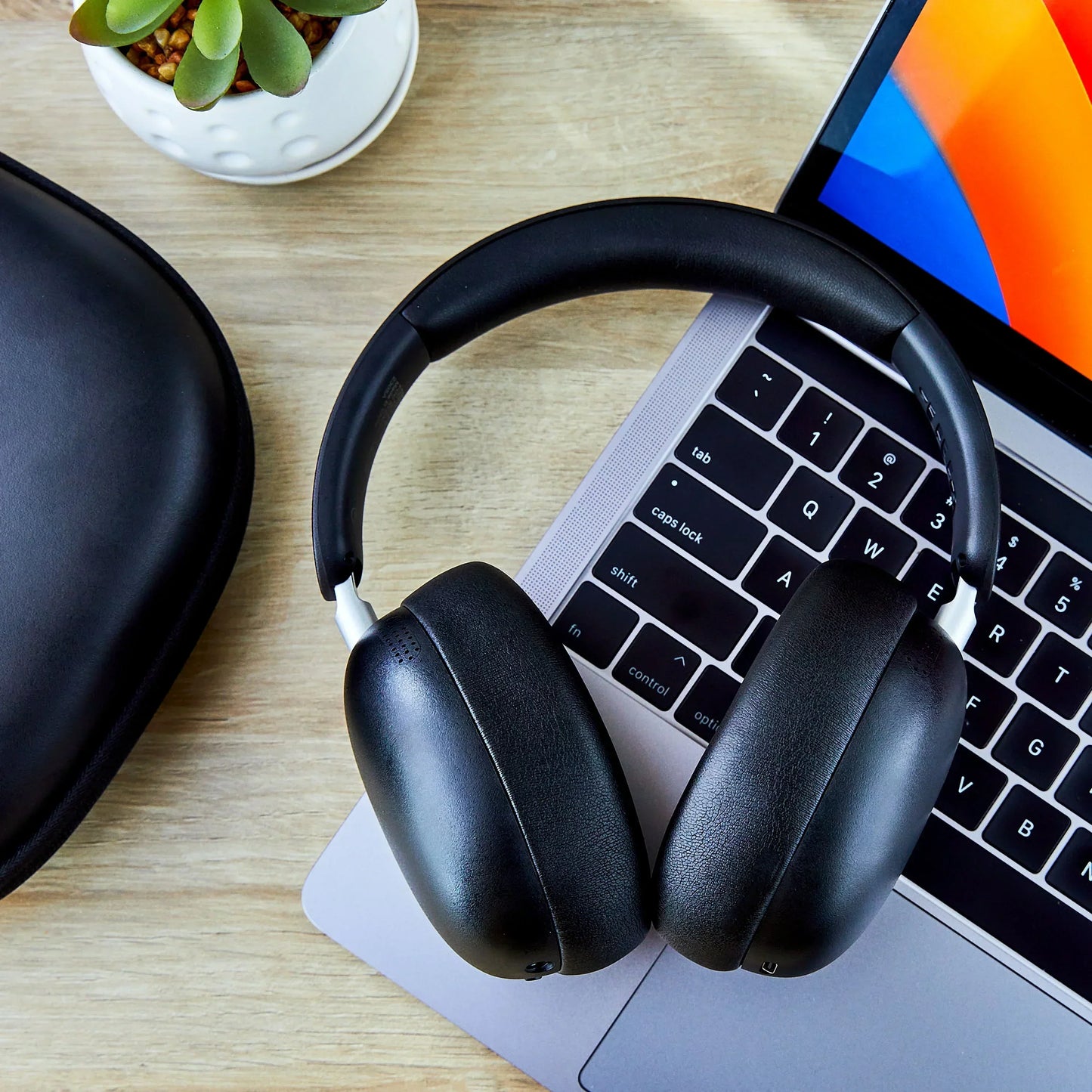 Black over-ear wireless headphones on a laptop keyboard beside a hard case and a small potted plant