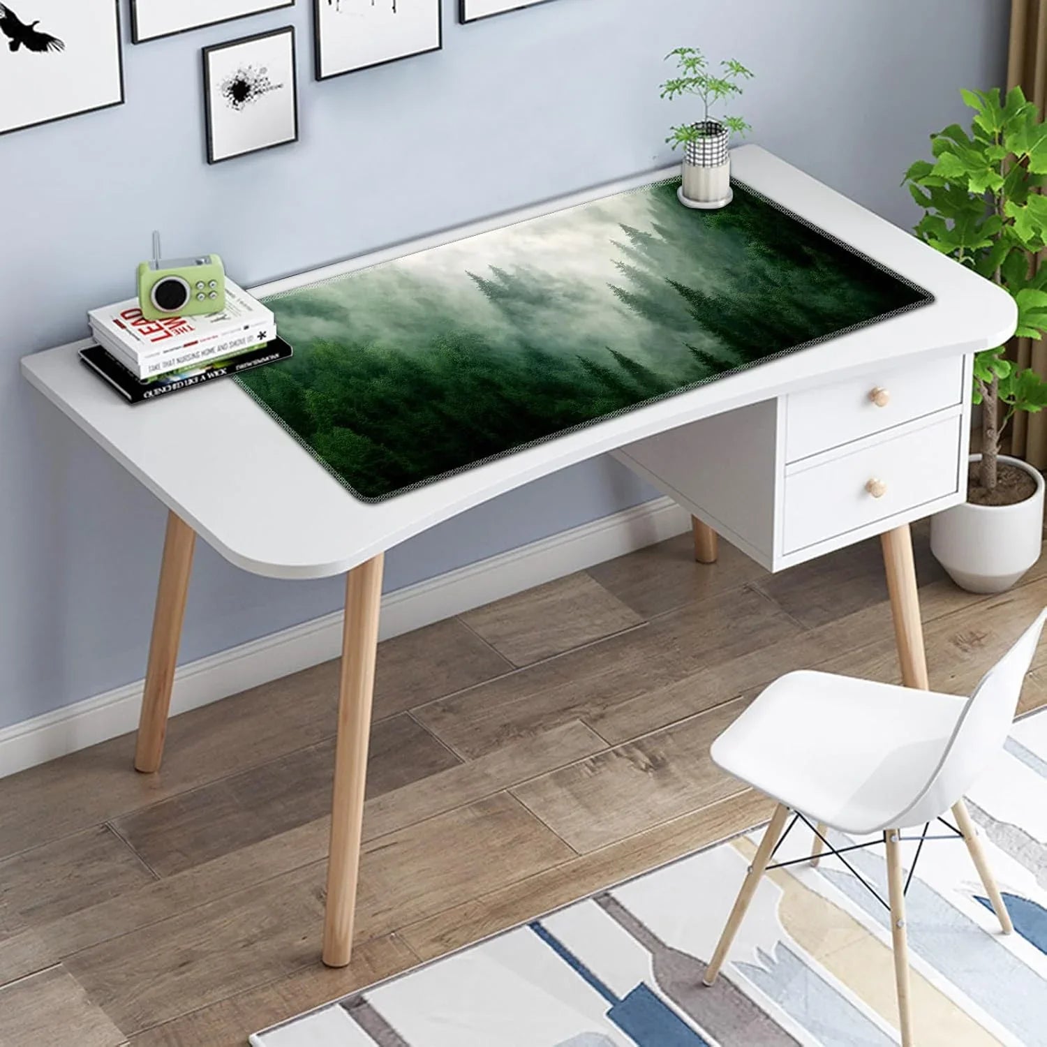 White modern desk with wooden legs featuring a large forest-themed gaming mouse pad and a small green radio on stacked books