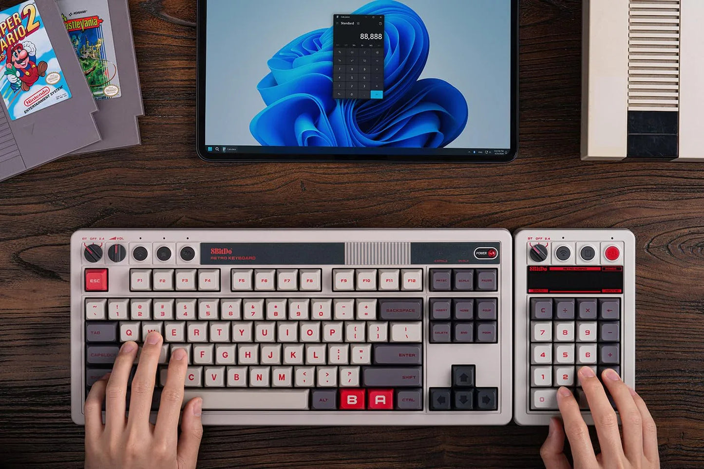 Hands using a retro gaming keyboard and numpad with a vintage computer setup on a wooden desk.