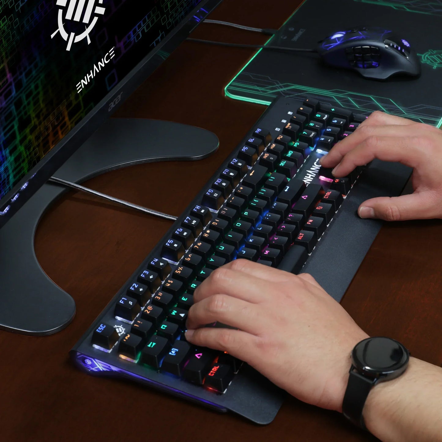Hands typing on RGB gaming keyboard with gaming mouse, monitor, and mousepad on desk