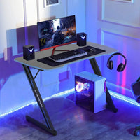 Modern gaming desk setup with curved monitor, RGB desktop PC, keyboard, mouse, speakers, and hanging headphones