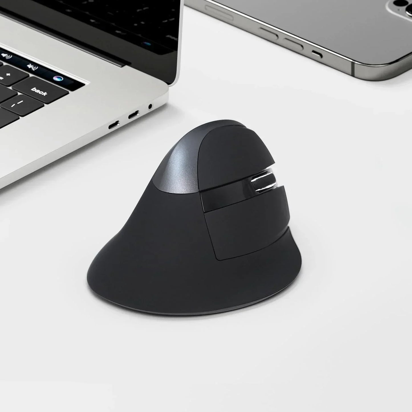 Ergonomic vertical wireless mouse on desk near laptop and smartphone, modern workspace accessory.