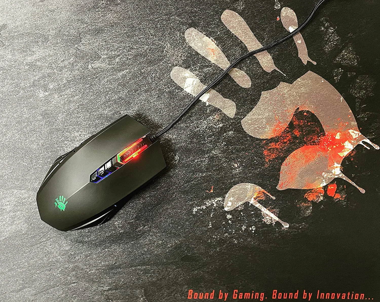 Black RGB gaming mouse with cord on black mouse pad featuring red and gray handprint graphic