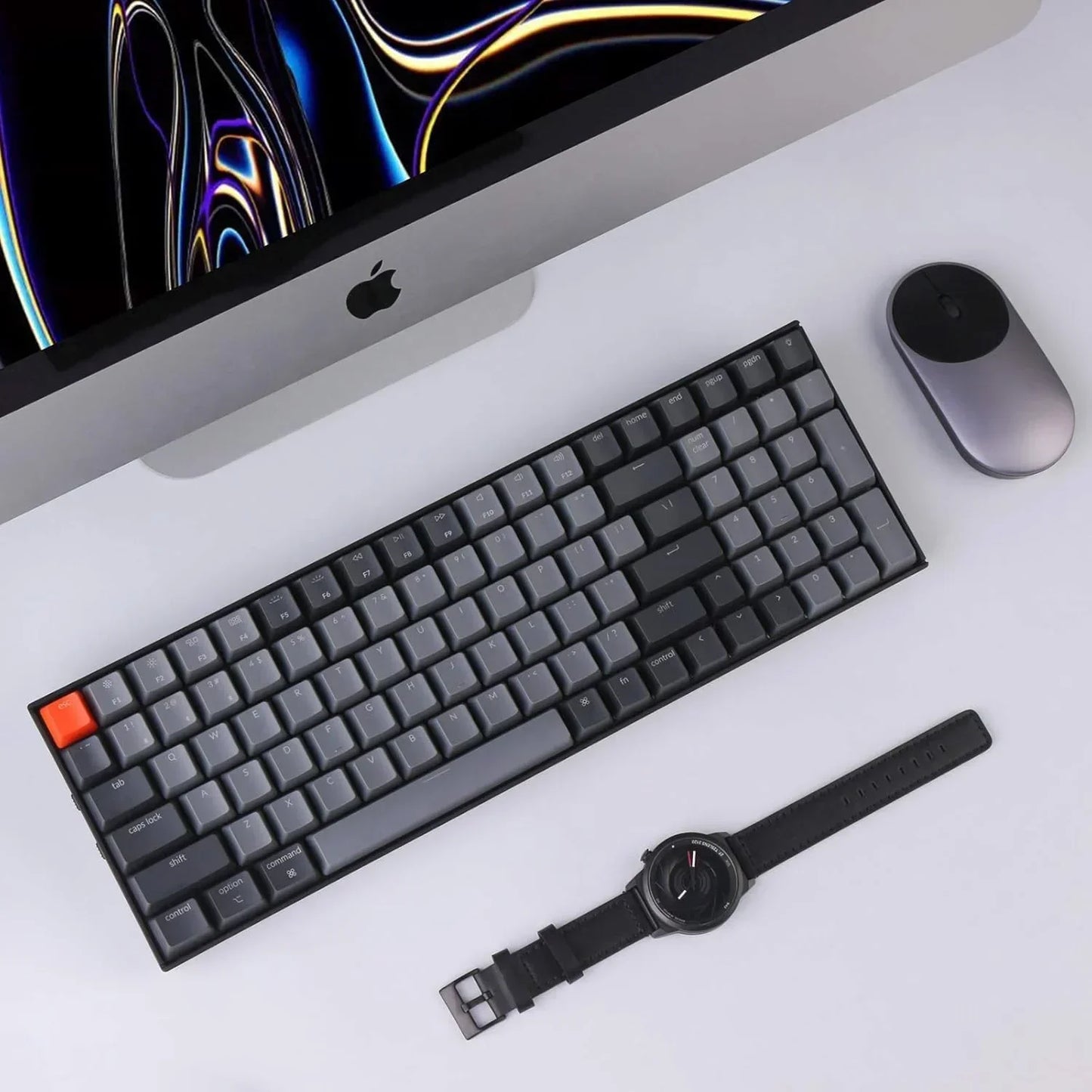 Modern gaming desk setup with mechanical keyboard, Apple iMac, mouse, and smartwatch