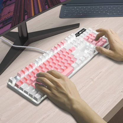 Person typing on white mechanical gaming keyboard with pink and white keycaps on a light wood desk