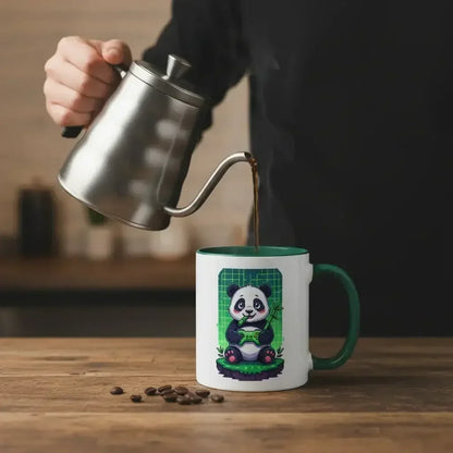 Hand pouring coffee from stainless steel kettle into white mug with green handle featuring cute panda design