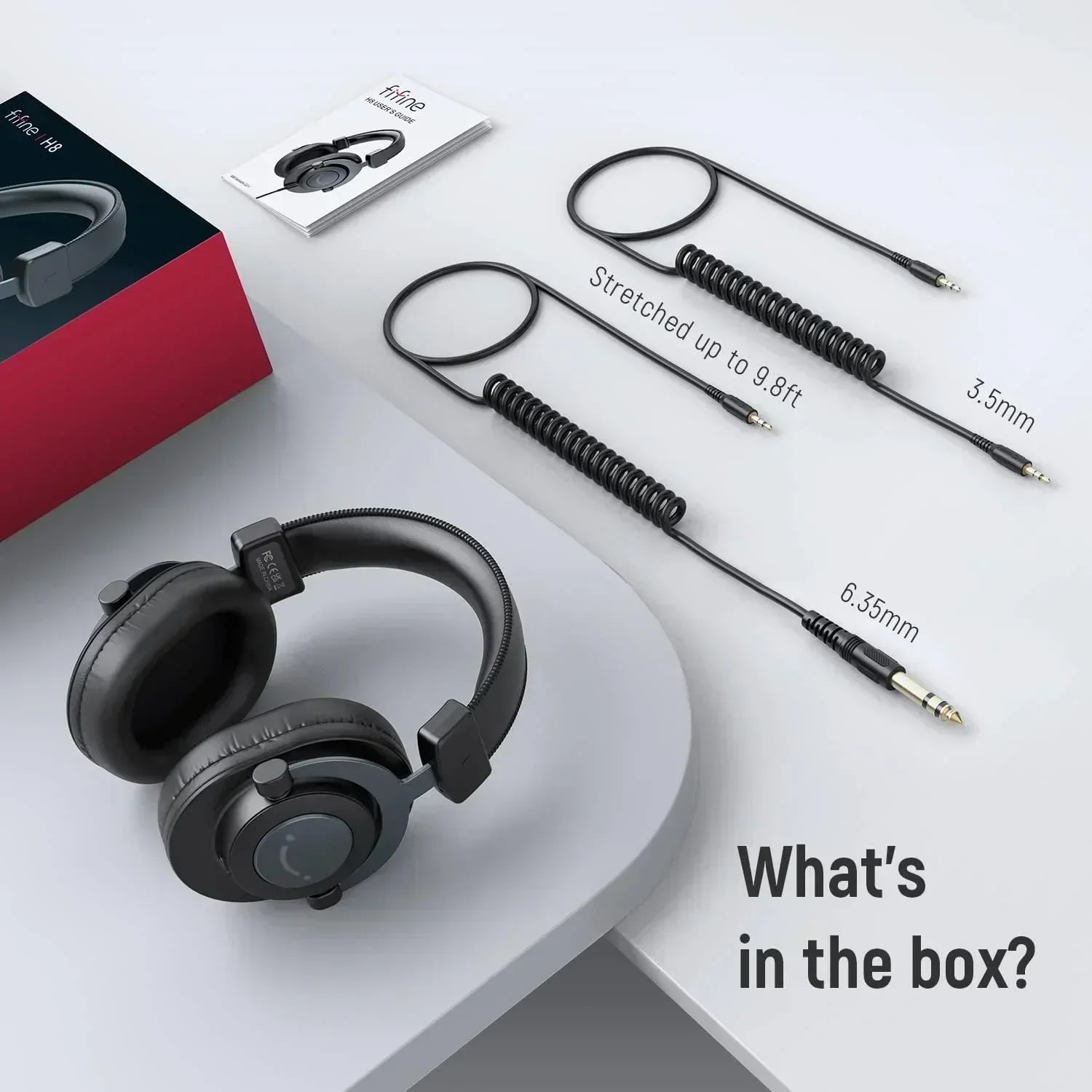 Gaming headset with coiled audio cables, 3.5mm and 6.35mm adapters, and user manual on a desk.