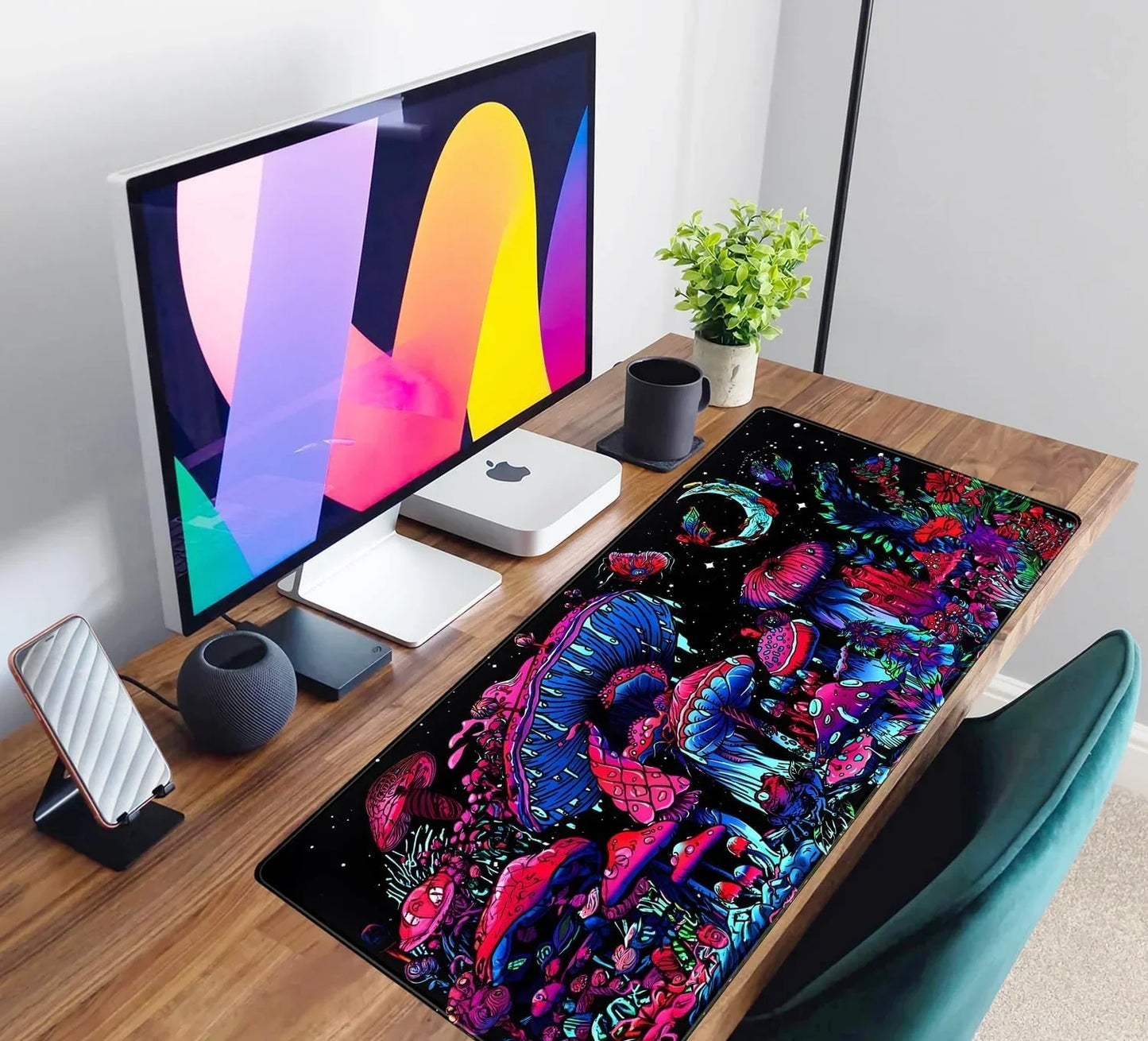 Modern desk setup with colorful psychedelic mushroom gaming mousepad, Apple Mac mini, monitor, and cup