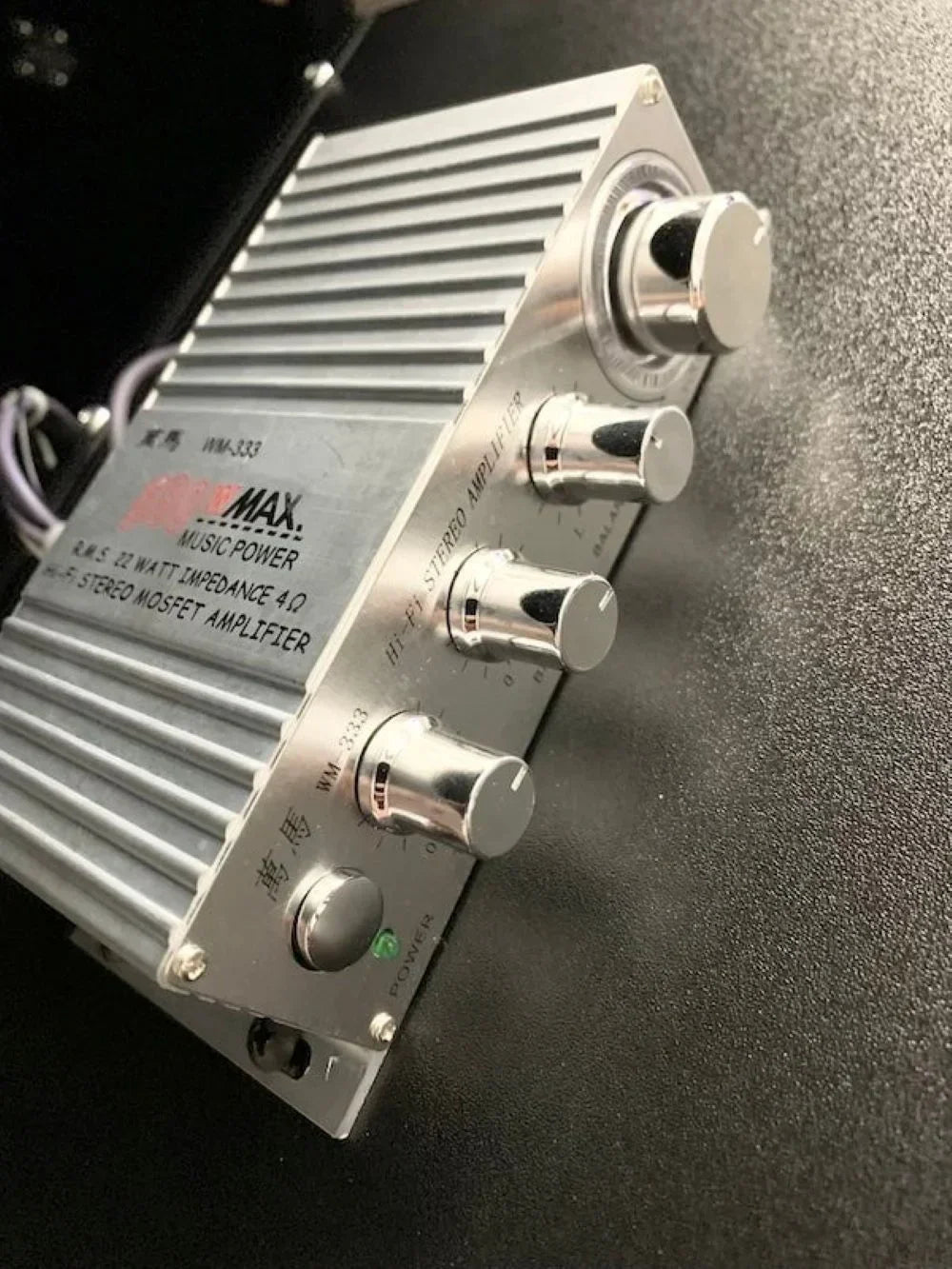Close-up of a silver stereo amplifier with control knobs on a black surface, retro gaming gear style