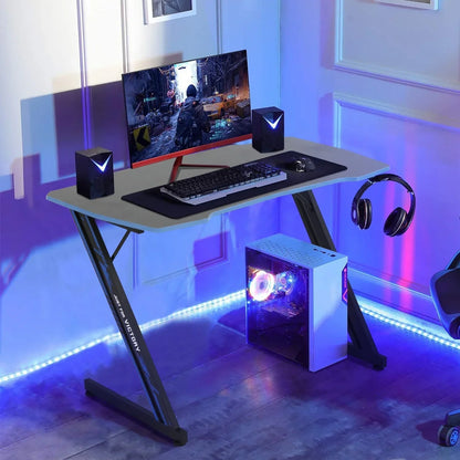 Modern gaming desk setup with PC tower, monitor, keyboard, mouse, speakers, and headphones