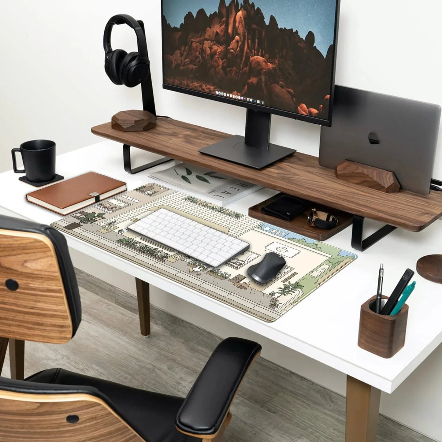 Modern white desk setup with wood monitor stand, large widescreen display, keyboard, mouse on illustrated desk mat, leather notebook, and headphones