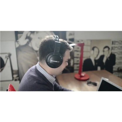 Man wearing black Koss headphones using a laptop at a gaming desk with a red lamp
