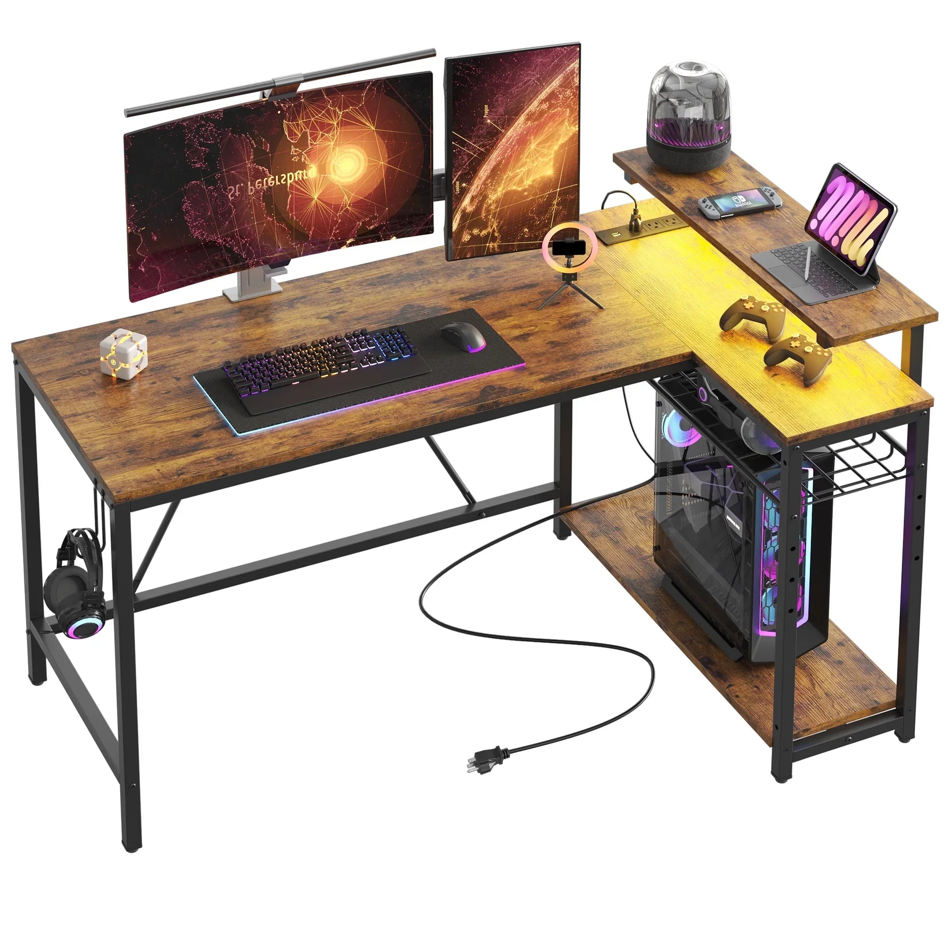 L-shaped wooden gaming desk with dual monitors, RGB keyboard, mouse, PC tower, controllers, and tablet setup