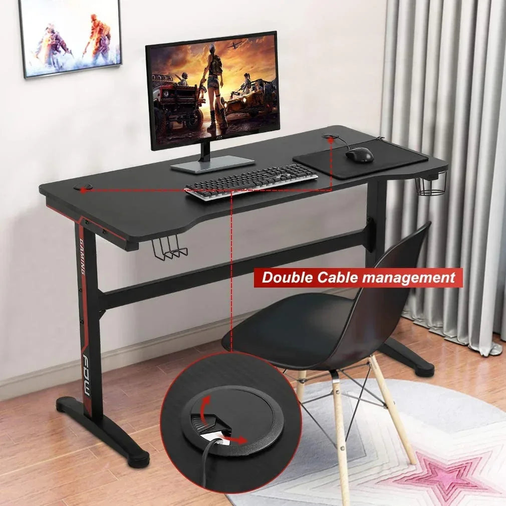 Black gaming desk with dual cable management, monitor, keyboard, mouse, and black chair on hardwood floor