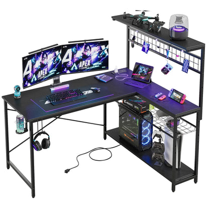 L-shaped black gaming desk with dual monitors, keyboard, mouse, PC tower, gaming console, tablets, controllers, and accessories