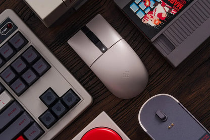 Modern wireless gaming mouse on desk with retro keyboard, game cartridge, and vintage gaming gear