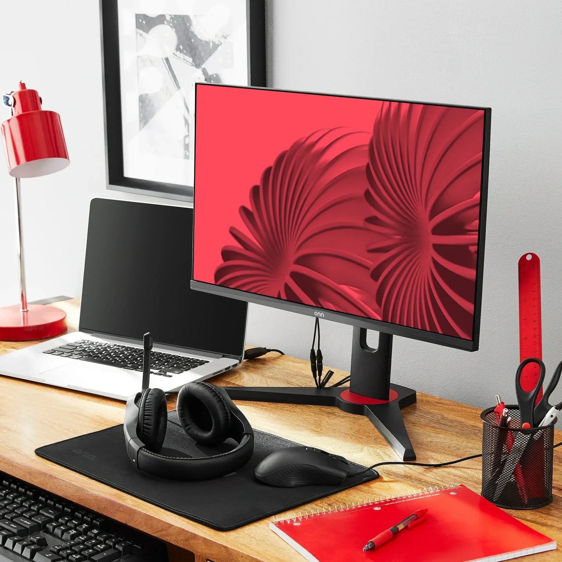 Modern gaming desk setup with dual monitors, black headset, mouse on mat, red lamp, and red desk accessories