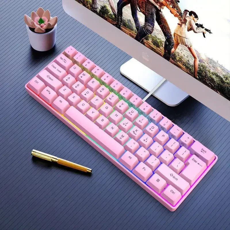 Pink compact mechanical gaming keyboard with RGB backlight on black desk beside monitor and pen