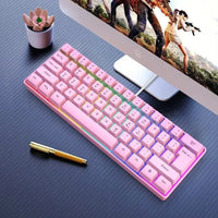 Pink compact mechanical gaming keyboard with RGB backlight on black desk beside monitor and pen