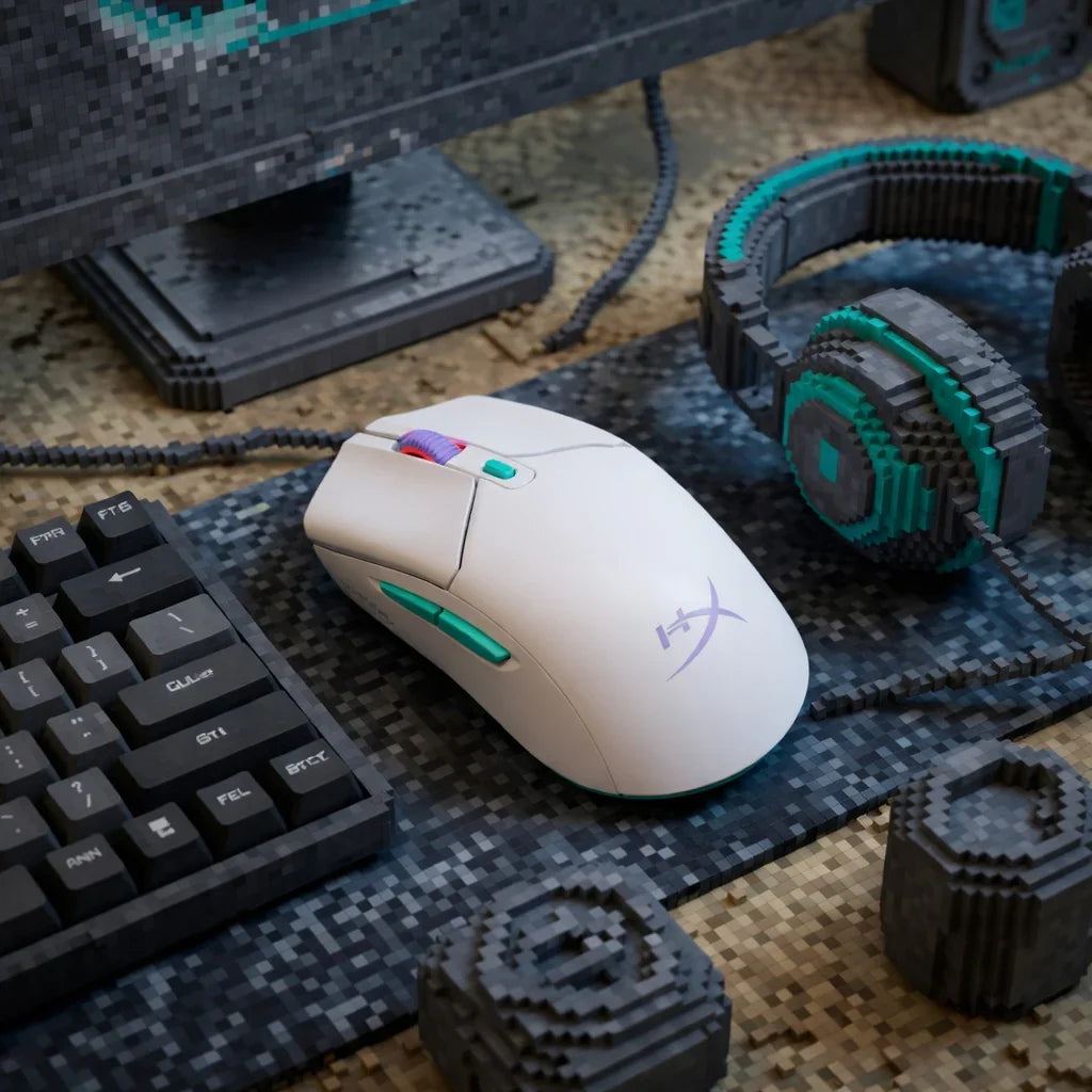 White gaming mouse with green accents on a pixel art desk, beside keyboard and headphones.