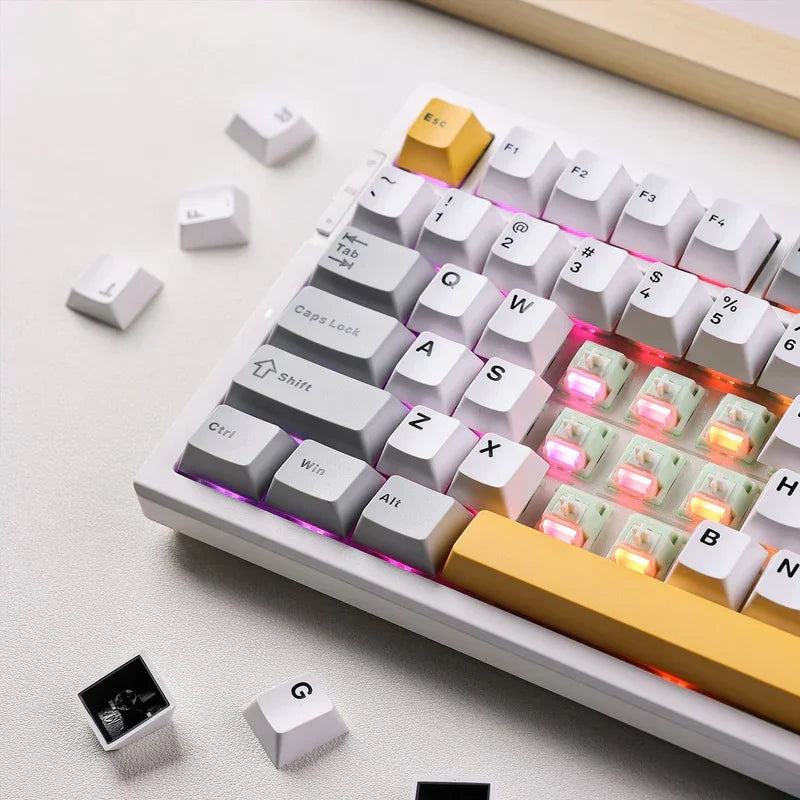 White mechanical gaming keyboard with RGB backlighting, yellow ESC key, and scattered keycaps on desk