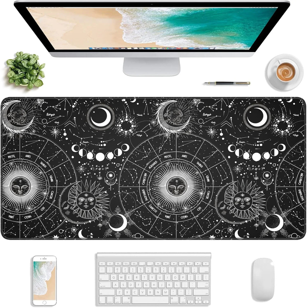 Astrology-themed black desk mat with zodiac signs and celestial designs under a computer, keyboard, mouse, phone, pen, plant, and coffee cup