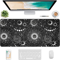 Astrology-themed black desk mat with zodiac signs and celestial designs under a computer, keyboard, mouse, phone, pen, plant, and coffee cup