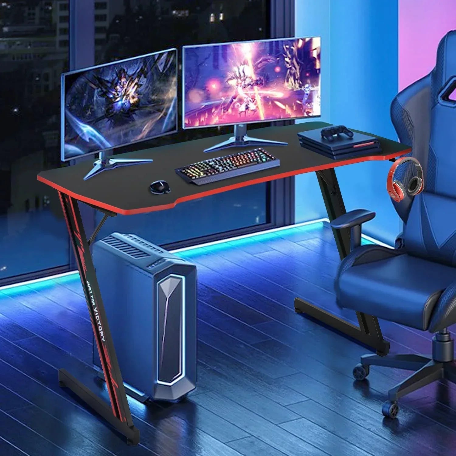 Modern black and red gaming desk setup with dual monitors, RGB keyboard, PC tower, headset, and gaming chair