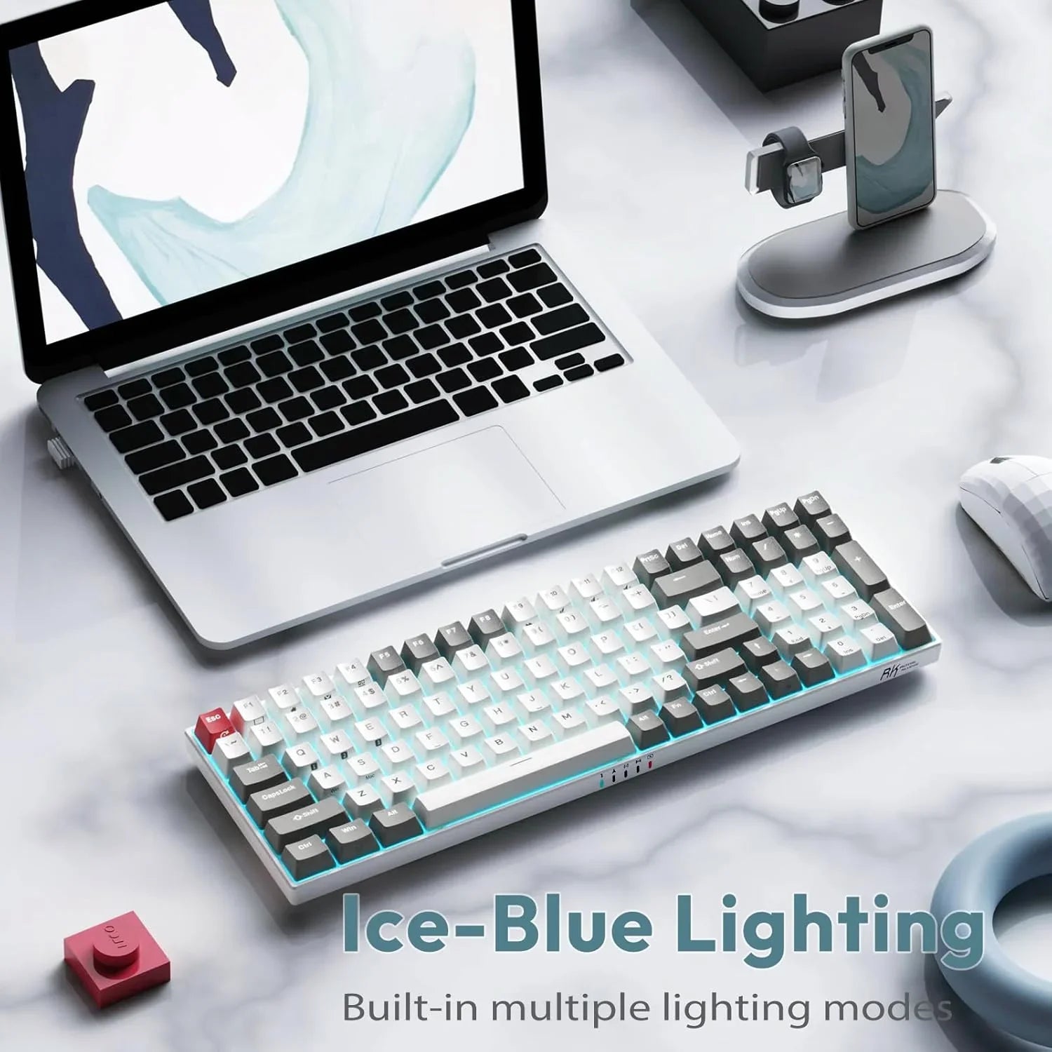 White and gray mechanical keyboard with ice-blue backlighting next to laptop and accessories on marble desk