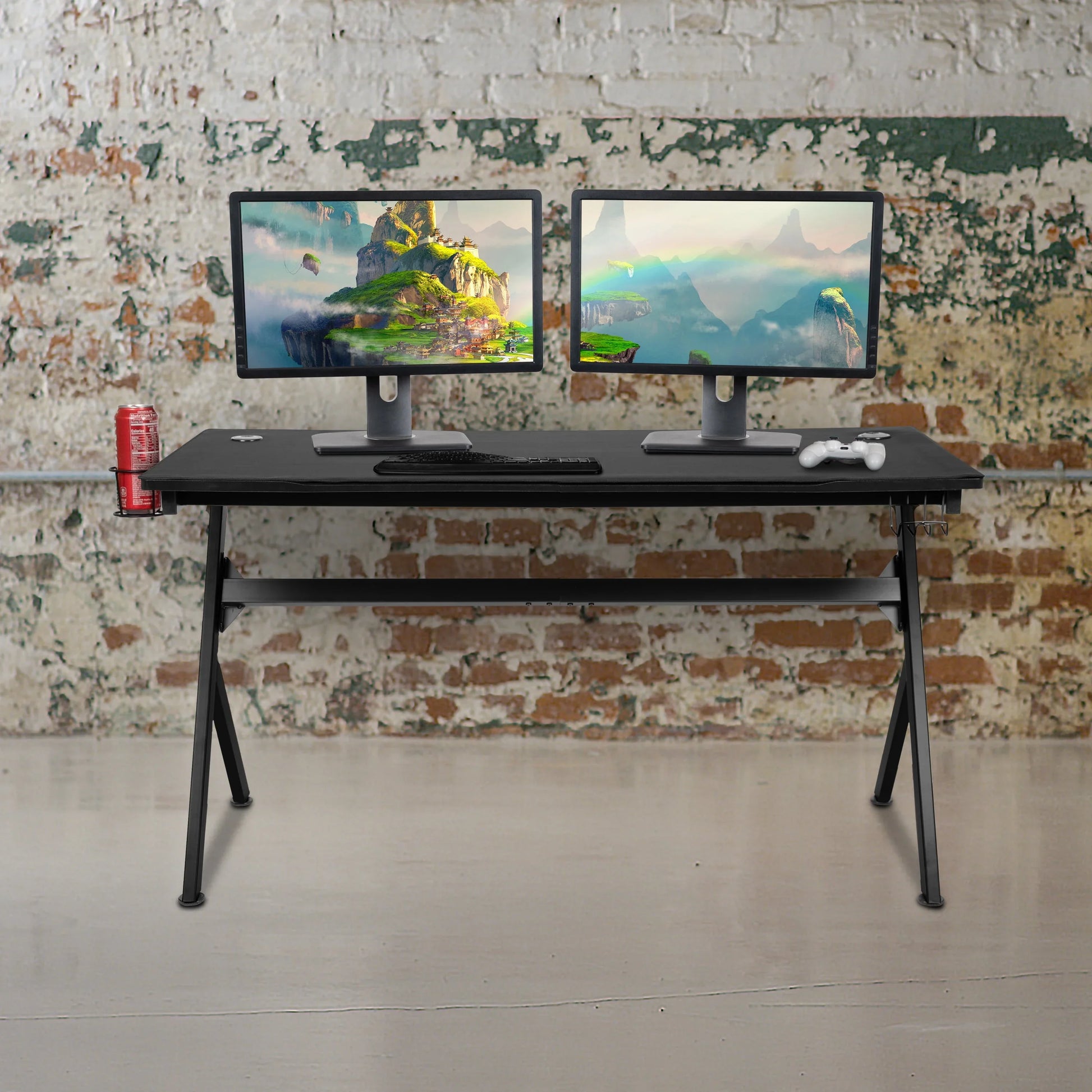 Black gaming desk with dual monitors, keyboard, game controller, and a red soda can holder against rustic brick wall