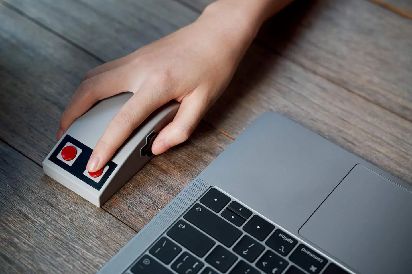 Hand using retro gaming mouse next to laptop on wooden desk