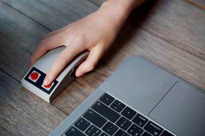 Hand using retro gaming mouse next to laptop on wooden desk