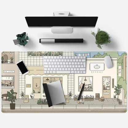 Top view of a clean desk with a monitor, keyboard, mouse, cute cartoon town-themed desk mat, smartphone, notebook, pen, and a small plant