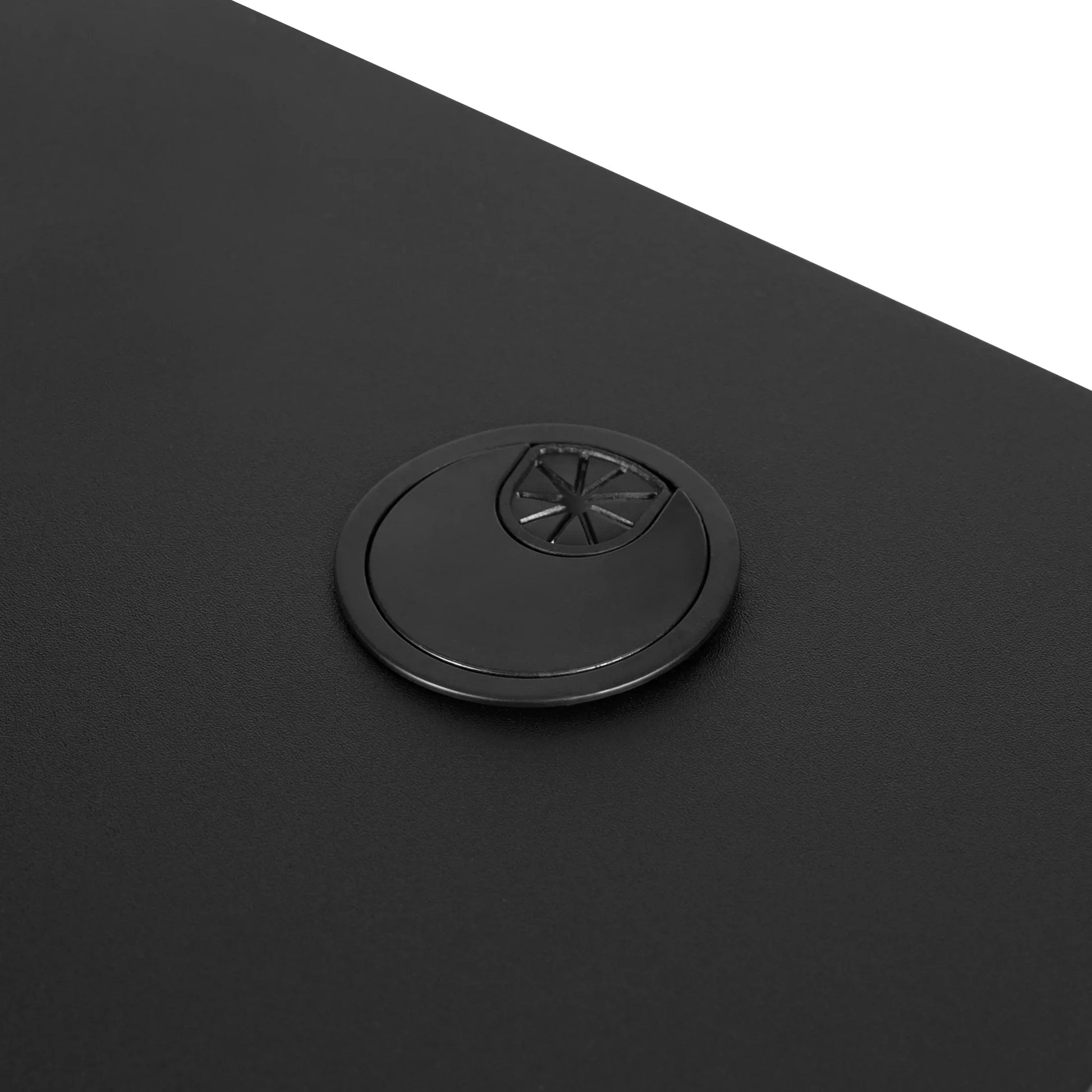 Black desk surface with a circular cable management grommet featuring slotted opening